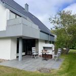 Terrasse mit Stuhl, Tisch und Strandkorb. Hintergrund: Haus mit Balkon und Grünfläche.