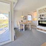 Wohn- und Essbereich mit TV, Tisch und Stühlen, Küche im Hintergrund, Terrasse mit Blick auf Garten.