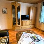 Wohnzimmer mit Holzmöbeln, Fernseher und Fenster mit Vorhängen.