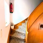 Holzgetreppe mit gemustertem Teppich, Feuerlöscher an der Wand und kleines Fenster.