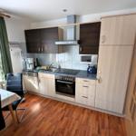 Küche mit Essbereich, Holzboden und Fenster mit Vorhängen.