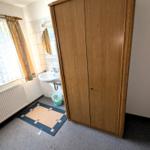 Zimmer mit Kleiderschrank, Waschbecken und Fenster mit Vorhängen.