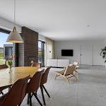 Großes Wohn- und Esszimmer mit Holztisch, Sitzgelegenheiten und Kamin. Blick auf grünen Garten.