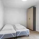 Zimmer mit zwei Einzelbetten, Kleiderschrank und Fenster mit Vorhang.