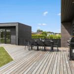 Terrasse mit Tisch, Stühlen und Grill. Hintergrund: modernes Haus mit Holzverkleidung.