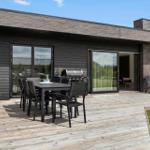 Terrasse mit Tisch, Stühlen und Grill. Durchgehende Glasfront zum Innenraum.