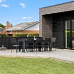 Terrasse mit Tisch, Stühlen und Grill neben modernem Haus mit Holz- und Ziegelsteinfassade.