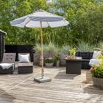 Deck with lounge furniture, umbrella, and plants. Wooden deck and trees in background.