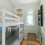 A bedroom with a white bunk bed, a window, and a bookshelf on the wall.