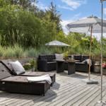 Deck with loungers, seating group, and umbrella. Surrounded by greenery and plants.