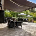 Deck with seating, grill, and awning. Background with greenery and flowers.