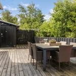 Deck with table and chairs, surrounded by trees and a wooden shed.