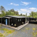 Black wooden house with blue door, deck, and garden. Surrounded by trees and grass.