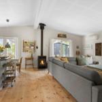 Living and dining area with wooden floor, fireplace, and large windows.