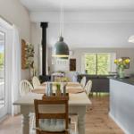 Dining area with table and chairs, living area with sofa and TV, large windows.