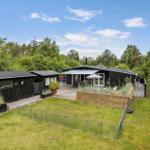 Black wooden cabin with terrace and garden. Surrounded by trees under blue sky.