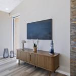 Wohnzimmer mit TV, Holzschrank und Steinwand. Terrasse mit Tischen und Stühlen.