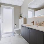 Badezimmer mit Doppelwaschbecken, Spiegel und Toilette. Tür führt nach draußen.