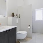 Bad mit Waschbecken, Toilette und Dusche. Goldfarbener Wasserhahn und Spiegelschrank.
