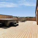 Terrasse mit Whirlpool, Tisch und Stühlen. Holzdecke und Holzwand. Blick auf Wald und Himmel.