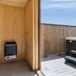 Sauna mit Holzwand und Heizgerät, Blick auf Terrasse mit Whirlpool und Holzgeländer.