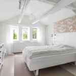 Schlafzimmer mit weißem Bett, Holzbalken und floraler Wandverkleidung.