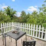 Terrasse mit weißem Zaun und schwarzem Tischset. Blick in grüne Bäume und blauen Himmel.