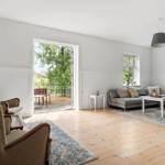 Wohnzimmer mit Sofa, Sessel und Terrasse. Holzboden und Fenster mit Blick auf Grün.