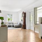 Wohnzimmer mit Sofa, Holzboden und Uhr. Küche mit Spülmaschine sichtbar.