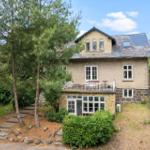 Ein zweistöckiges Haus mit Balkon und Garten. Umgeben von Bäumen und Sträuchern.
