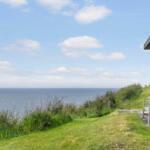 Haus mit Blick auf das Meer, grüner Rasen und Bank vor der Wand.
