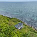 Kleines Haus auf einer grünen Halbinsel direkt am Meer mit Blick auf Windkraftanlagen.