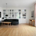 Wohnzimmer mit Sofa, Couchtisch und Holzboden. Große Fenster und Tür führen nach draußen.