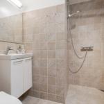 Bad mit Dusche, Waschbecken und Toilette. Fliesenwand und Spiegel sichtbar.