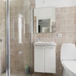 Badezimmer mit Dusche, Waschbecken und Toilette. Fliesenwand und Spiegelschrank.