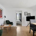 Wohn- und Essbereich mit grünen Sesseln, Holztisch und Fernseher. Durchgang zur Schlafzimmer.