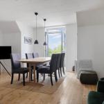 Essbereich mit Tisch, Stühlen und TV. Tür führt auf Balkon. Holzboden und weiße Wände.