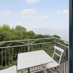 Balkon mit weißem Tisch und Stühlen, Blick auf Meer und grüne Bäume.