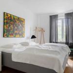 Schlafzimmer mit Bett, Nachttisch, Stuhl und Fenster mit Vorhängen.