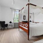 Schlafzimmer mit Holzboden, Bett mit Baldachin und Sessel.