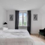 Schlafzimmer mit großem Bett, Fenster mit Blick auf Grün, dunkler Sessel und Wandbild.
