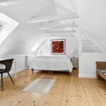 Schlafzimmer mit Dachschrägen, Schreibtisch, Bett und Rattanbank.