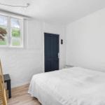 Schlafzimmer mit weißer Wand, Bett, Fenster und Holzständer.