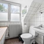 Badezimmer mit Toilette, Waschbecken und Fenster. Weiße Fliesen und Holzbank.