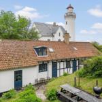 Wohnhaus mit rotem Ziegeldach und blauen Türen. Im Hintergrund Leuchtturm. Grünanlagen und Grillplatz.