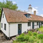 Wohnhaus mit rotem Dach und grünen Fensterrahmen, im Hintergrund Leuchtturm.