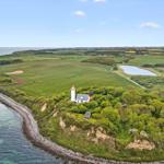 Lichtturm auf einer grünen Halbinsel mit Feldern und Meer.