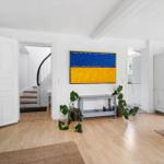Wohnraum mit Holzboden, weißer Tür, Treppe und Wandbild