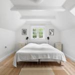 Schlafzimmer mit Dachbodenfenster, Holzboden und weißem Bett.