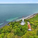 Lichtturm auf Küstenrücken mit grünen Wiesen und Meer im Hintergrund.